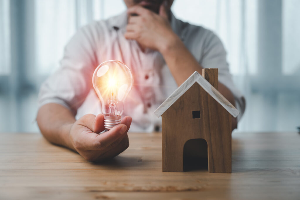 Male hand touching a light bulb with house model on desk. the concept of installment and reduction of home loan interest, saving energy and money concept. idea for buying a house.